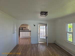 Unfurnished dining area featuring baseboard heating, dark wood-style floors, crown molding, arched walkways, and a textured ceiling