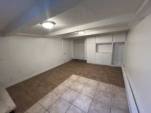 Unfurnished bedroom featuring light tile patterned flooring, a baseboard heating unit, beamed ceiling, a textured ceiling, and a closet