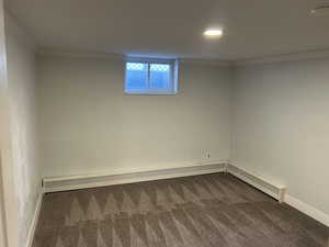 Basement with crown molding, dark colored carpet, a baseboard heating unit, and a baseboard radiator