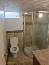 Full bathroom featuring tile walls, a stall shower, vanity, and light tile patterned floors