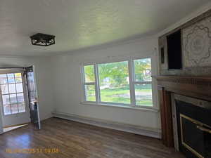 Unfurnished living room featuring a baseboard heating unit, dark wood-style floors, a tile fireplace, a textured ceiling, and ornamental molding