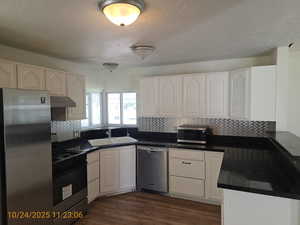 Kitchen with stainless steel appliances, backsplash, a textured ceiling, under cabinet range hood, and dark wood-style flooring