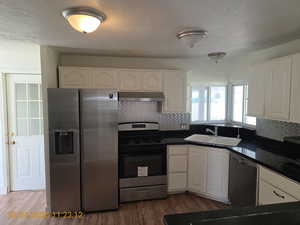 Kitchen featuring appliances with stainless steel finishes, tasteful backsplash, a textured ceiling, under cabinet range hood, and dark wood finished floors