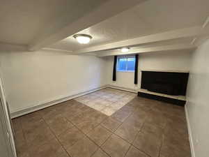 Below grade area featuring tile patterned floors, a textured ceiling, a baseboard radiator, and a fireplace with raised hearth