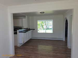 Kitchen with arched walkways, dark wood-style flooring, dark countertops, crown molding, and backsplash