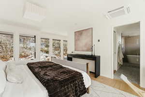 Bedroom with cooling unit, light wood finished floors, and connected bathroom