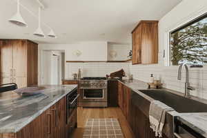 Kitchen with high end stainless steel range, backsplash, dark stone counters, light wood-style floors, and modern cabinets
