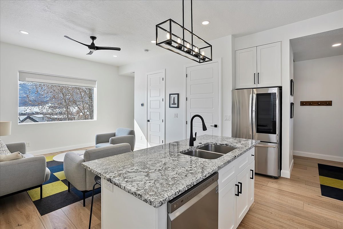 Kitchen featuring open floor plan, stainless steel appliances, light wood finished floors, light stone counters, and white cabinets