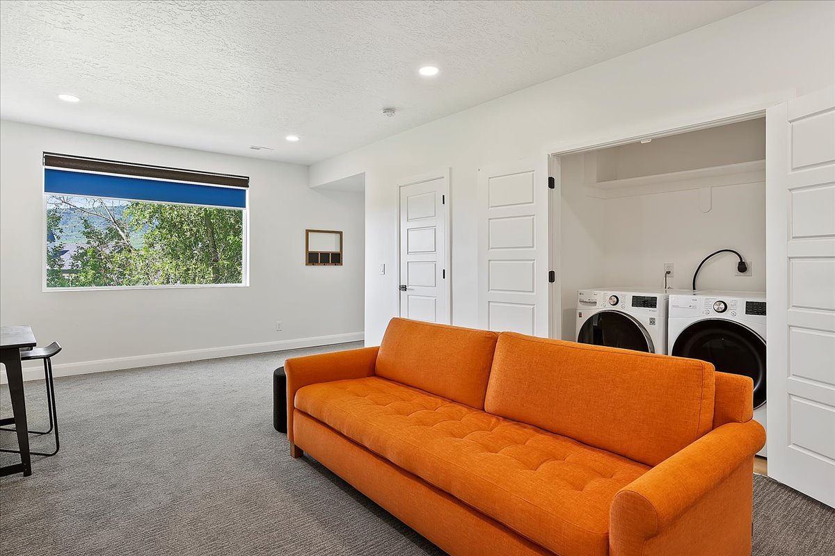 Living room with carpet flooring, a textured ceiling, recessed lighting, and washing machine and dryer