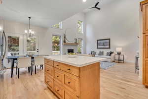 Kitchen with open floor plan, a kitchen island, light wood-type flooring, hanging light fixtures, and a towering ceiling