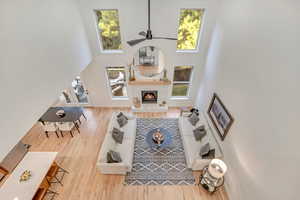 From balcony overlooking living area with a high ceiling, wood finished floors, a fireplace, healthy amount of natural light, and ceiling fan