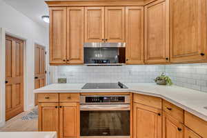 Kitchen with stainless steel appliances, tasteful backsplash, light stone counters, and light wood-type flooring