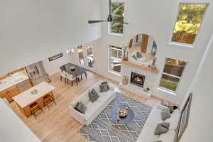 Living room with a towering ceiling, light wood-style flooring, a fireplace, and a ceiling fan
