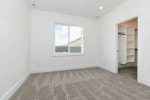 Unfurnished bedroom featuring light carpet, a walk in closet, and recessed lighting