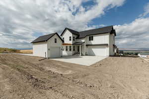 View of front of home with board and batten siding, dirt driveway, an outdoor structure, and a shingled roof