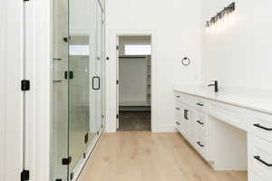 Bathroom with vanity, a walk in closet, a stall shower, and light wood finished floors