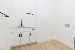 Washroom featuring light wood finished floors, washer hookup, and cabinet space