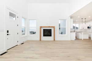 Unfurnished living room with light wood-style flooring, a fireplace, a high ceiling, and recessed lighting