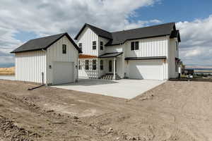 Modern inspired farmhouse featuring driveway, a shingled roof, board and batten siding, an outdoor structure, and an attached garage