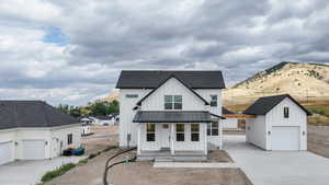 Modern farmhouse featuring board and batten siding, an outbuilding, covered porch, a shingled roof, and a standing seam roof