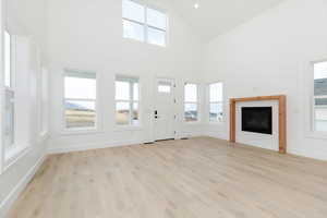 Unfurnished living room featuring high vaulted ceiling, light wood-style flooring, and a fireplace