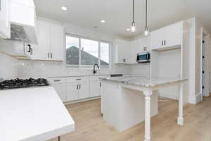 Kitchen featuring decorative backsplash, a breakfast bar, pendant lighting, white cabinets, and recessed lighting