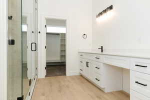Bathroom featuring vanity, light wood finished floors, a spacious closet, and a shower stall