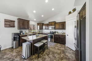 Kitchen featuring dark brown cabinets, stainless steel appliances, lofted ceiling, a breakfast bar area, and a kitchen island