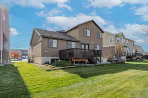 Rear view of property featuring a wooden deck, stucco siding, a yard, and a residential view