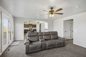 Carpeted living room with a textured ceiling, arched walkways, a ceiling fan, and a chandelier