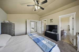 Carpeted bedroom with lofted ceiling, ceiling fan, connected bathroom, and tile patterned floors