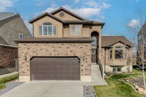 View of front of house with driveway, a garage, brick siding, stucco siding, and a front yard