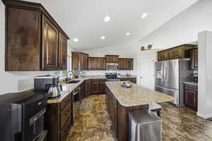 Kitchen featuring dark brown cabinetry, appliances with stainless steel finishes, vaulted ceiling, a breakfast bar, and a kitchen island
