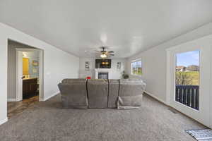 Living area with a glass covered fireplace, dark colored carpet, a ceiling fan, and a textured ceiling