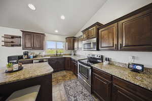 Kitchen featuring dark brown cabinetry, vaulted ceiling, stainless steel appliances, light stone countertops, and recessed lighting