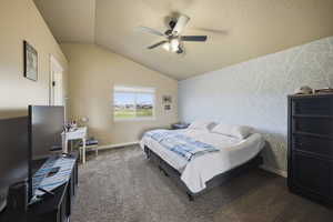 Carpeted bedroom featuring wallpapered walls, vaulted ceiling, ceiling fan, a textured ceiling, and an accent wall