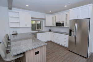 Kitchen with light stone counters, appliances with stainless steel finishes, white cabinets, open shelves, and recessed lighting
