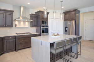 Kitchen with wall chimney exhaust hood, a breakfast bar area, stainless steel appliances, tasteful backsplash, and light wood-style floors
