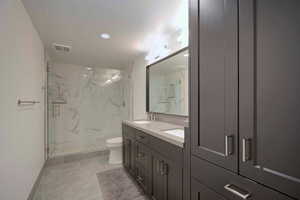 Bathroom with double vanity, a marble finish shower, and recessed lighting