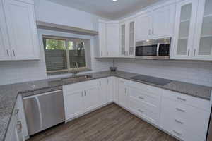 Kitchen with white cabinets, stainless steel appliances, light stone countertops, and dark wood-type flooring