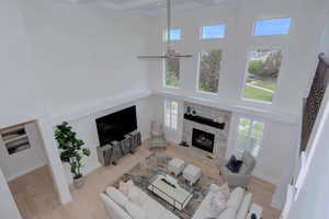 Living area with a towering ceiling, a stone fireplace, ceiling fan, wood finished floors, and plenty of natural light
