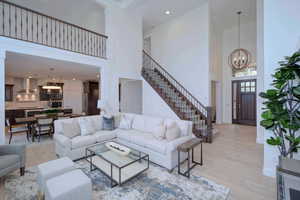Living area featuring light wood-style flooring, a towering ceiling, stairs, a chandelier, and recessed lighting