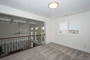 Empty room with coffered ceiling, beamed ceiling, carpet, and ceiling fan