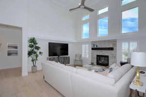 Living area with a high ceiling, light wood-style flooring, plenty of natural light, ceiling fan, and a fireplace