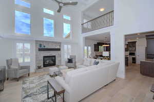 Living room with light wood-style floors, a ceiling fan, a towering ceiling, recessed lighting, and a fireplace