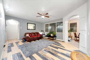 Living room with arched walkways, a ceiling fan, and light wood-style floors