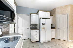 Kitchen featuring electric range, dark countertops, white fridge with ice dispenser, and stainless steel microwave