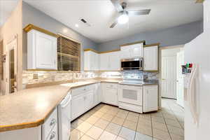 Kitchen with white appliances, light tile patterned floors, backsplash, and white cabinets