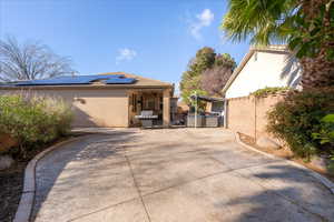 View of side of property featuring stucco siding, solar panels, and a patio