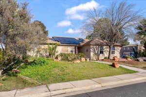 View of front facade with a front yard, stucco siding, and solar panels